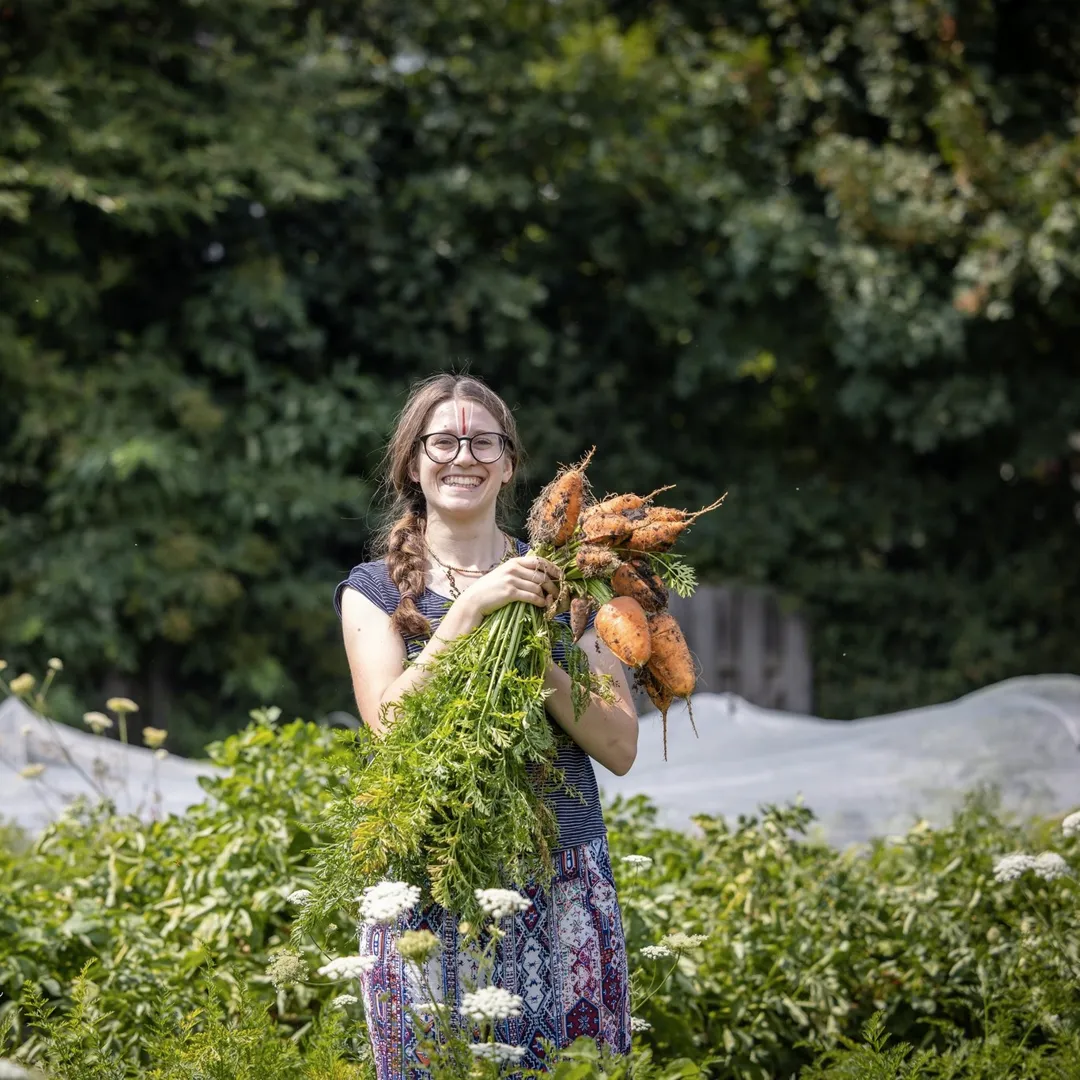 person smiling while harvesting vegetables in the garden